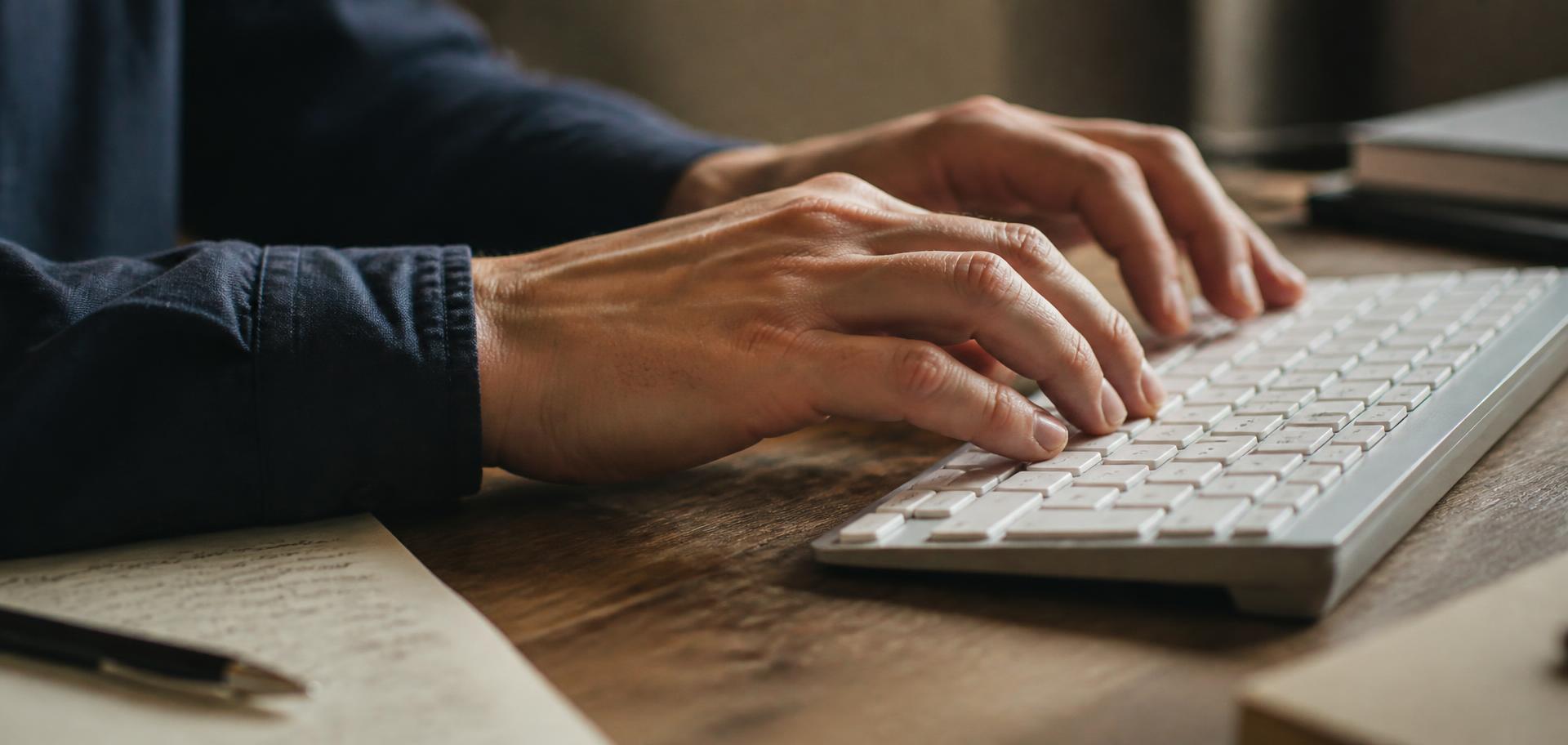 Hände auf einer Tastatur an der Schreibtischkante bei warmem Licht